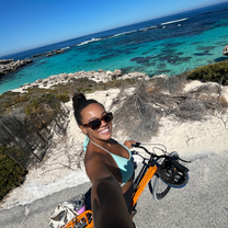 A girl on a bike taking a selfie with a blue sea behind her.