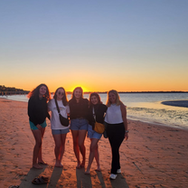 A group of girls posing for a photo on the beach at sunset