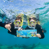 Two girls posing underwater with a sign that shows they are at the Great Barrier Reef