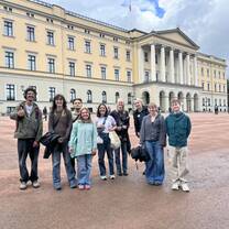 a group of college students stand smiling in front of the royal castle in oslo