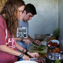 Two volunteers prepare fresh vegetables in a kitchen as part of a farm to table school meal program.