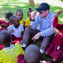 Volunteer sitting on the ground with primary school children, engaging them in conversation and play during a school visit