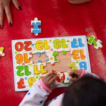 A close-up shot of a young child's hands carefully placing the final letter into a colorful wooden alphabet puzzle on a classroom desk.