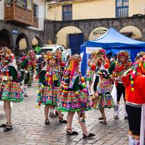 Locals dressed in bright, ceremonial Andean clothing gather in a historic city square for a traditional festival, surrounded by the colonial architecture of Peru.