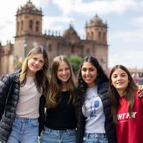 A group of four teen volunteers enjoying a sunny day in Cusco’s main square, standing before the iconic colonial church building during their trip to Peru.