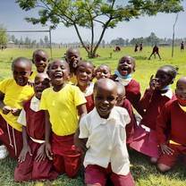 Group of primary school students in school uniforms sitting on grass, smiling and laughing during outdoor play time at Maisha Academy.