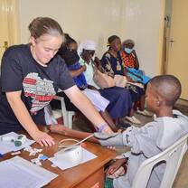 Volunteer measuring a patient’s blood pressure while patients wait for care inside the clinic