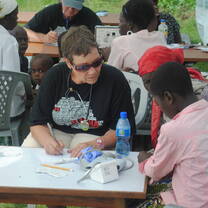 Volunteer clinician seated at an outdoor table recording patient information during a community medical outreach
