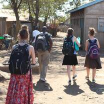 A group of volunteers and a local guide walk through a rural village pathway during a community visit.