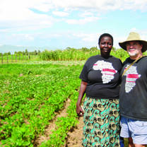 A Maisha Project staff member and an international partner standing in a cultivated farm plot used for community agriculture and school meal production in western Kenya.