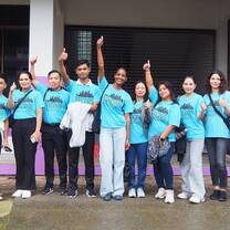 A diverse group of Kids English Thailand summer interns posing together in branded teal shirts during a regional outreach English camp.
