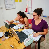 TEFL trainees planning lessons using laptops and printed materials in classroom.