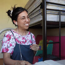 Smiling female TEFL teacher in bedroom teaching English online.