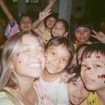 TEFL teacher smiles with her eyes closed, taking a selfie with a group on young students