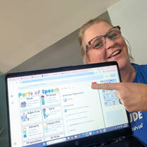 Female TEFL teacher points to laptop screen, it is showing teaching resources.