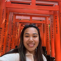 Smiling woman visiting Fushimi Inari Taisha in Kyoto, Japan, a famous site known for its thousands of vermilion coloured torii gates.