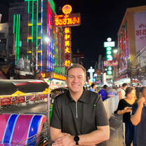 Man smiles at the camera on Yaowarat Road in Bangkok's, neon signs and lights can be seen behind him.