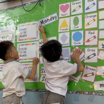 Two young students moving laminated cards on a wall board.