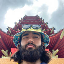 Young man in bucket hat and sunglasses stands in front on a red temple.