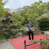 A student posing on a red bridge with greenery all around