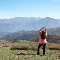 girl standing in front of mountains making a heart with her hands