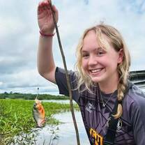 young girl holding up a fish that she caught in the Amazon