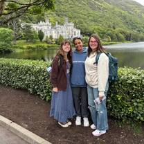 three girls standing together in front of a lake