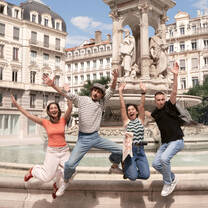 four people jumping in front of a historic fountain