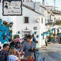 people eating on the street amidst white and blue buildings