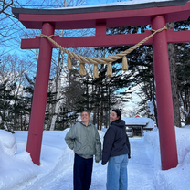Two women standing underneath a torii gate in the snow