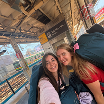 Two women at a train station in Japan with backpacks on their back