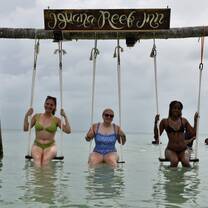 Three teen travelers sitting on a swing in the ocean in Belize