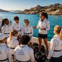 Illustrative image of a sailing coach briefing a team by the water in Sardinia
