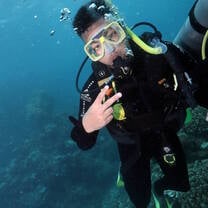 Jayden in Australia scuba diving underwater, wearing diving gear and posing his fingers in deuces
