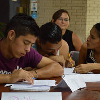 People working with worksheets around a wooden table.