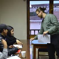A man holding paper and a marker beside seated learners and a wooden table.