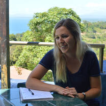 A woman seated at a table with an open notebook, facing another person.