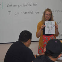 A woman holding a hand-drawn tree poster in front of a whiteboard.