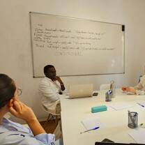 A classroom group sits facing a whiteboard with English lesson notes.