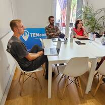 Participants sit around a classroom table with laptops and notebooks.