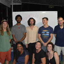 Eight people posing in front of a whiteboard.