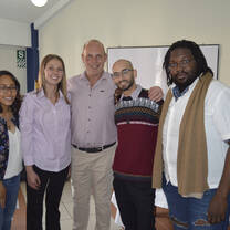 Five people smiling together in front of a whiteboard.