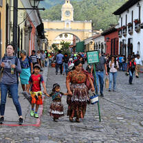 Pedestrians on a cobbled street beneath a yellow clock arch.