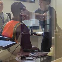 A woman is putting headphones on an airport worker in order to perform a hearing test. 