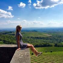 A woman sits on a wall above Tuscan vineyards in Siena.