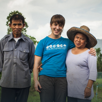 A smiling American student stands with a Thai couple who are also smiling