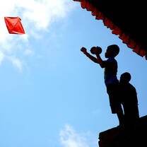Child plays with Kyte of top of a roof on a bright blue sky